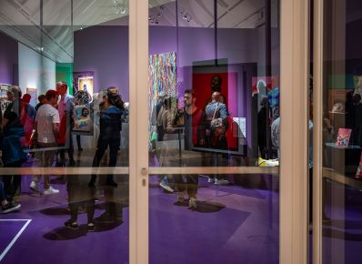 Personen in einer Ausstellung durch eine Glastür fotografiert, die Werke spiegeln sich im Glas